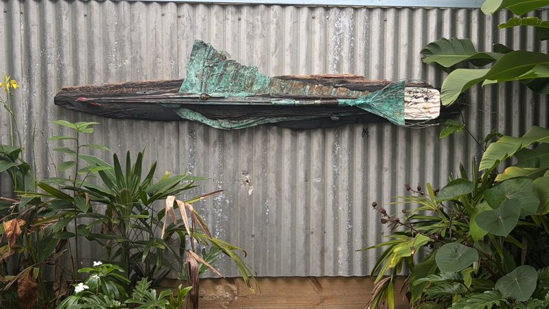 The handcrafted copper and timber sailfish hanging on the corrugated iron fence in The Sailfish Garden